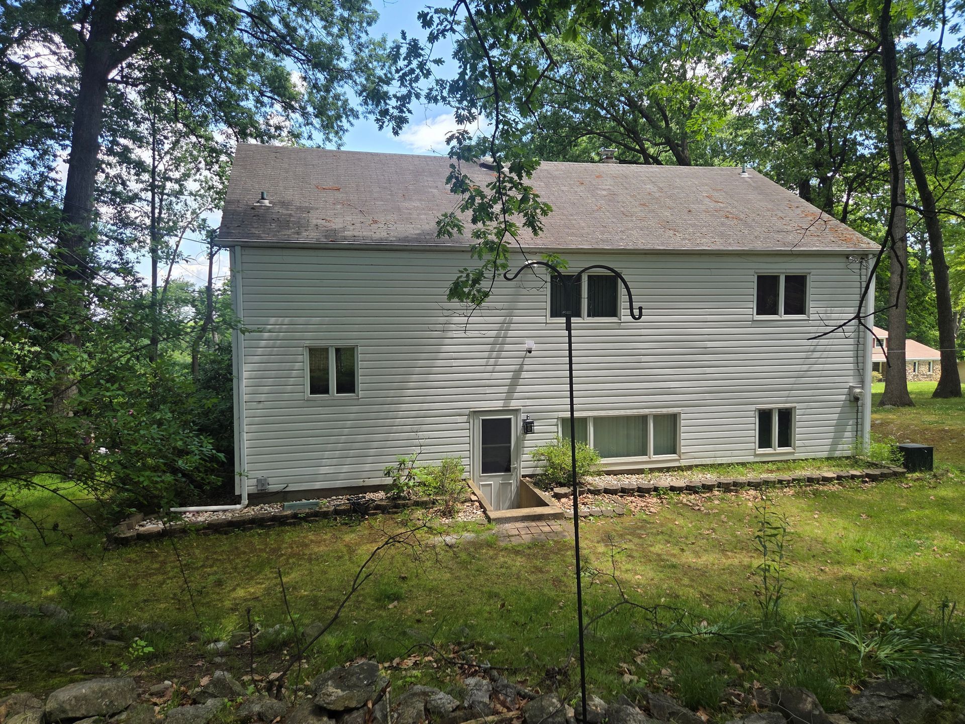White two-story house with a small front door, windows, and a yard surrounded by trees