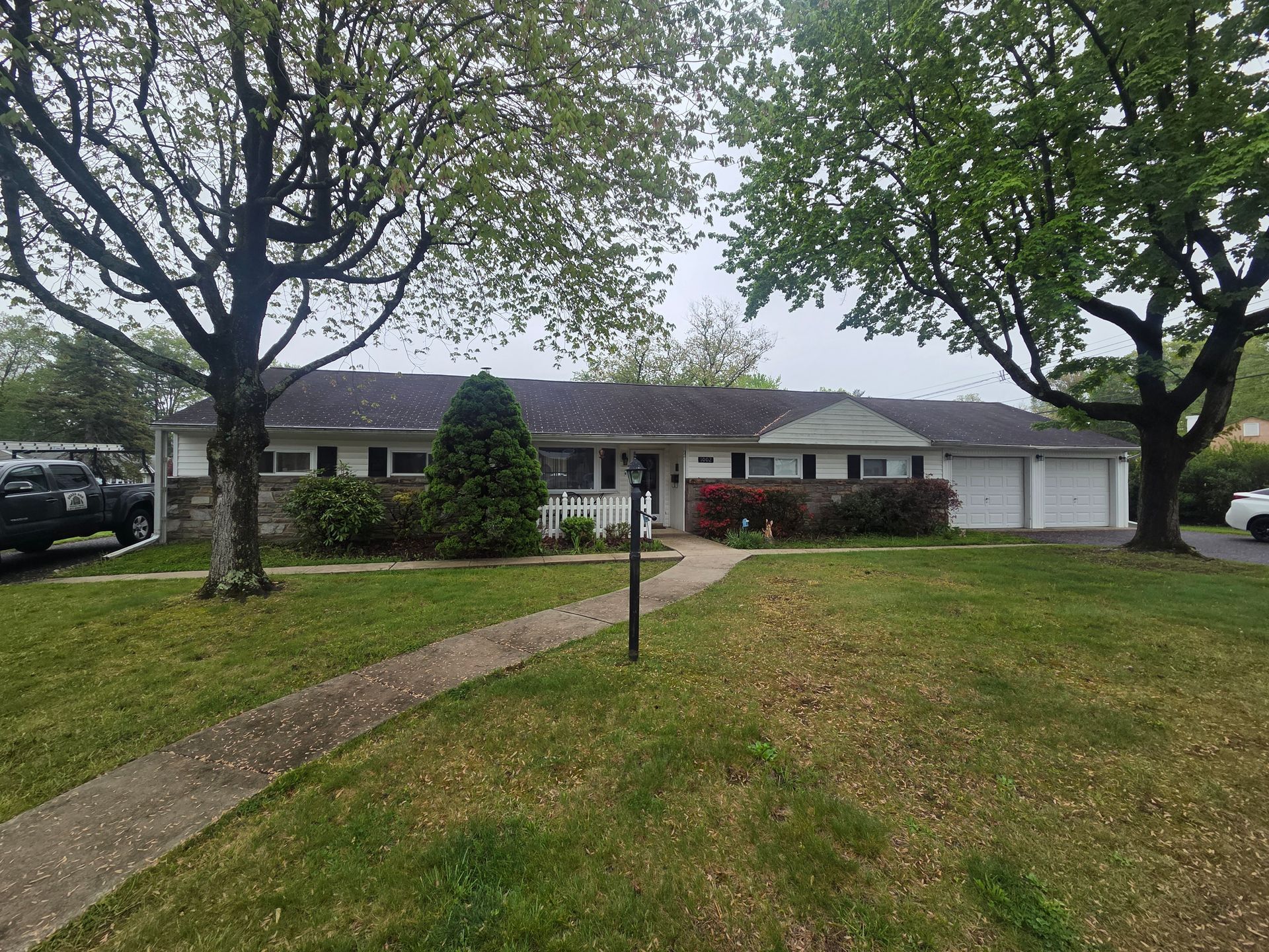 Single-story house with a front lawn, walkway, trees, and a double garage on the right