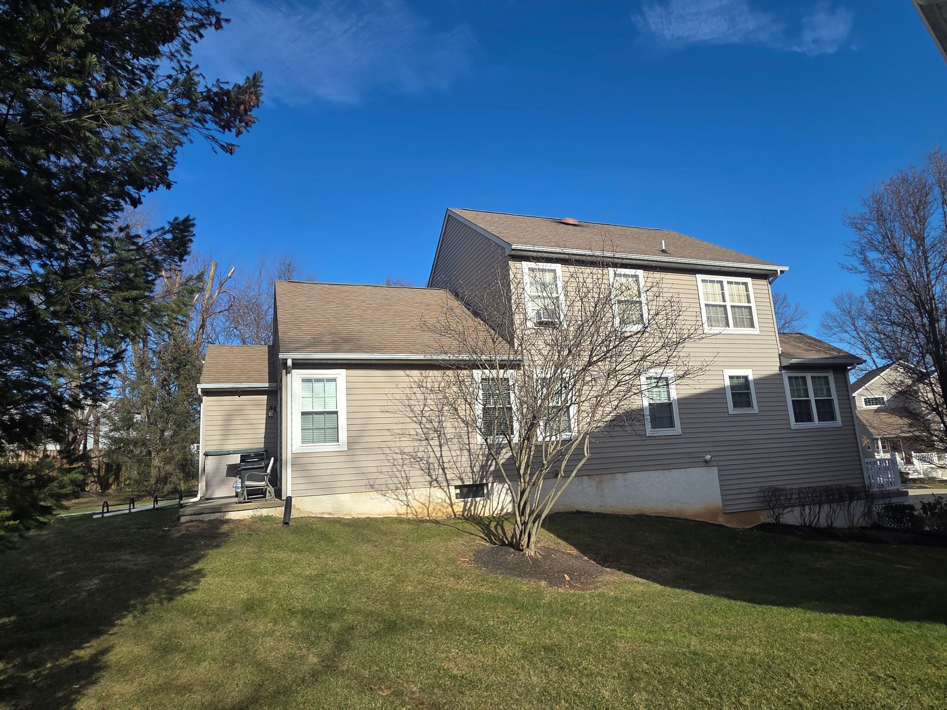 Suburban house with beige siding and stone facade, front lawn, and blue sky on a sunny day