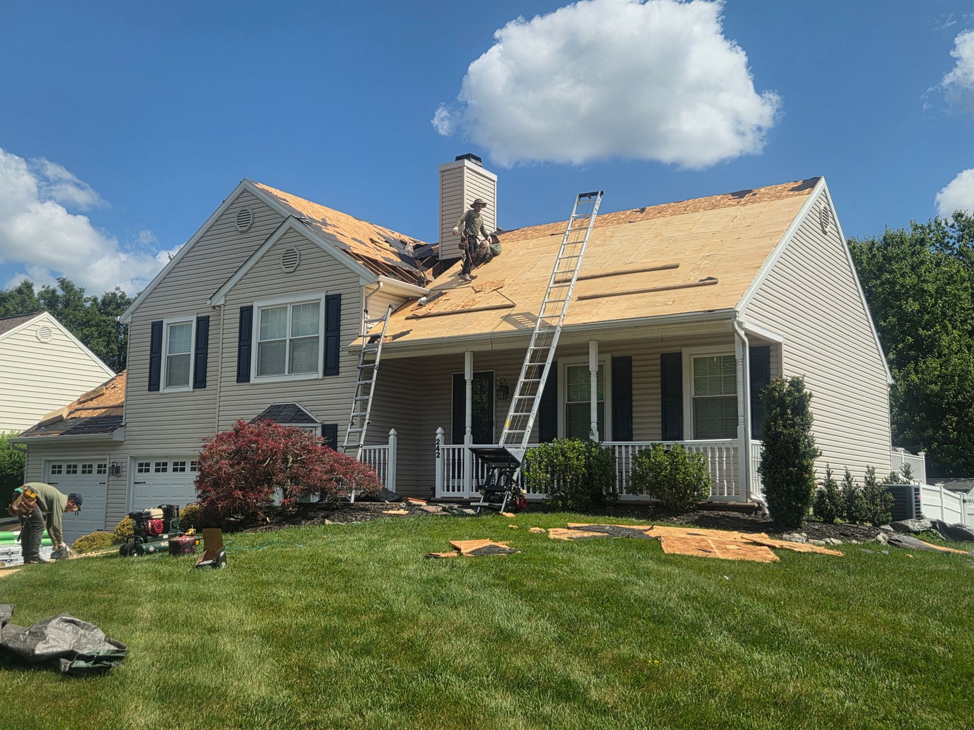 House with roof under repair, ladders leaning against it, on a sunny suburban lawn