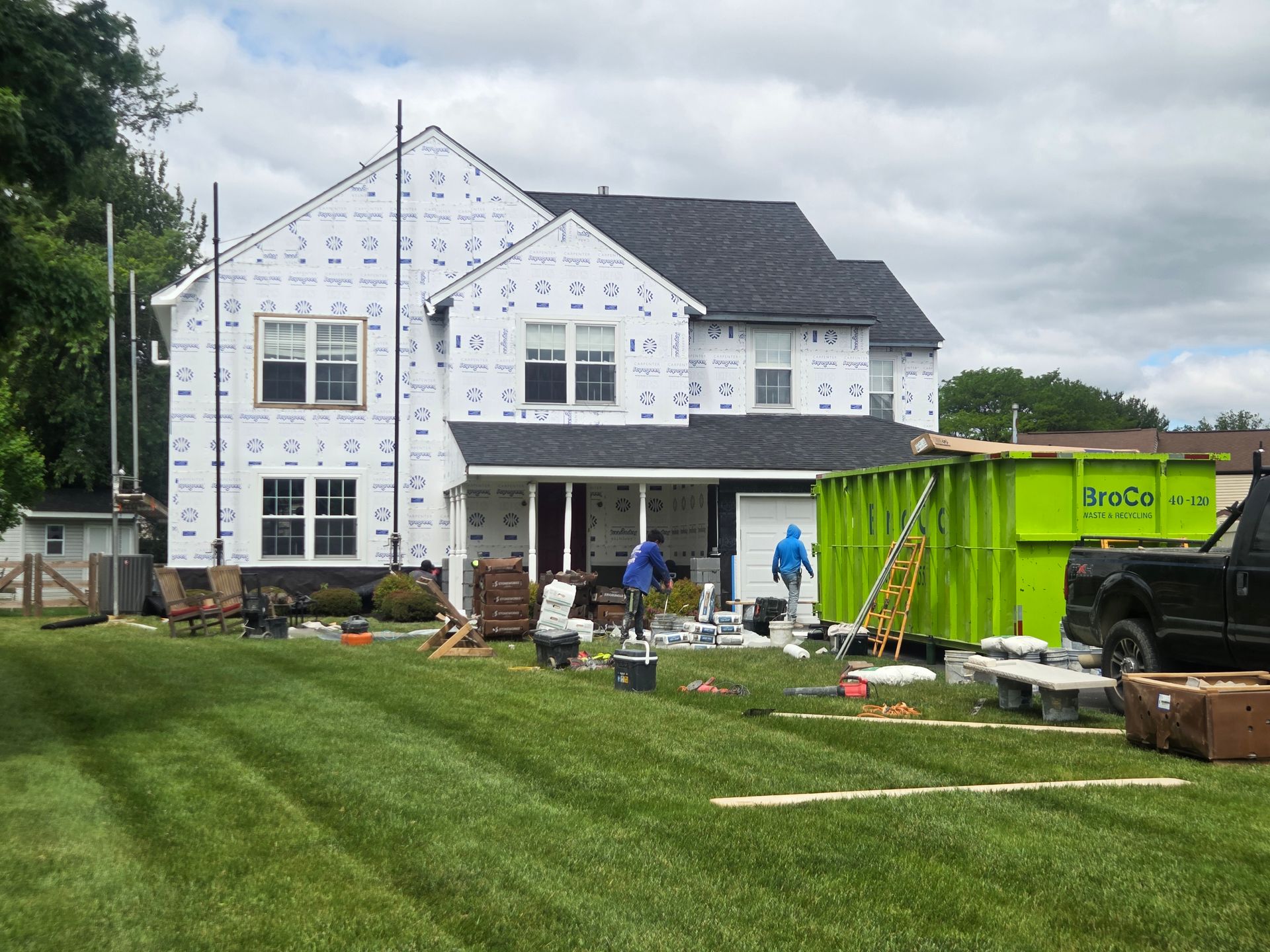 New house under construction with workers, white siding, and green dumpster in front yard