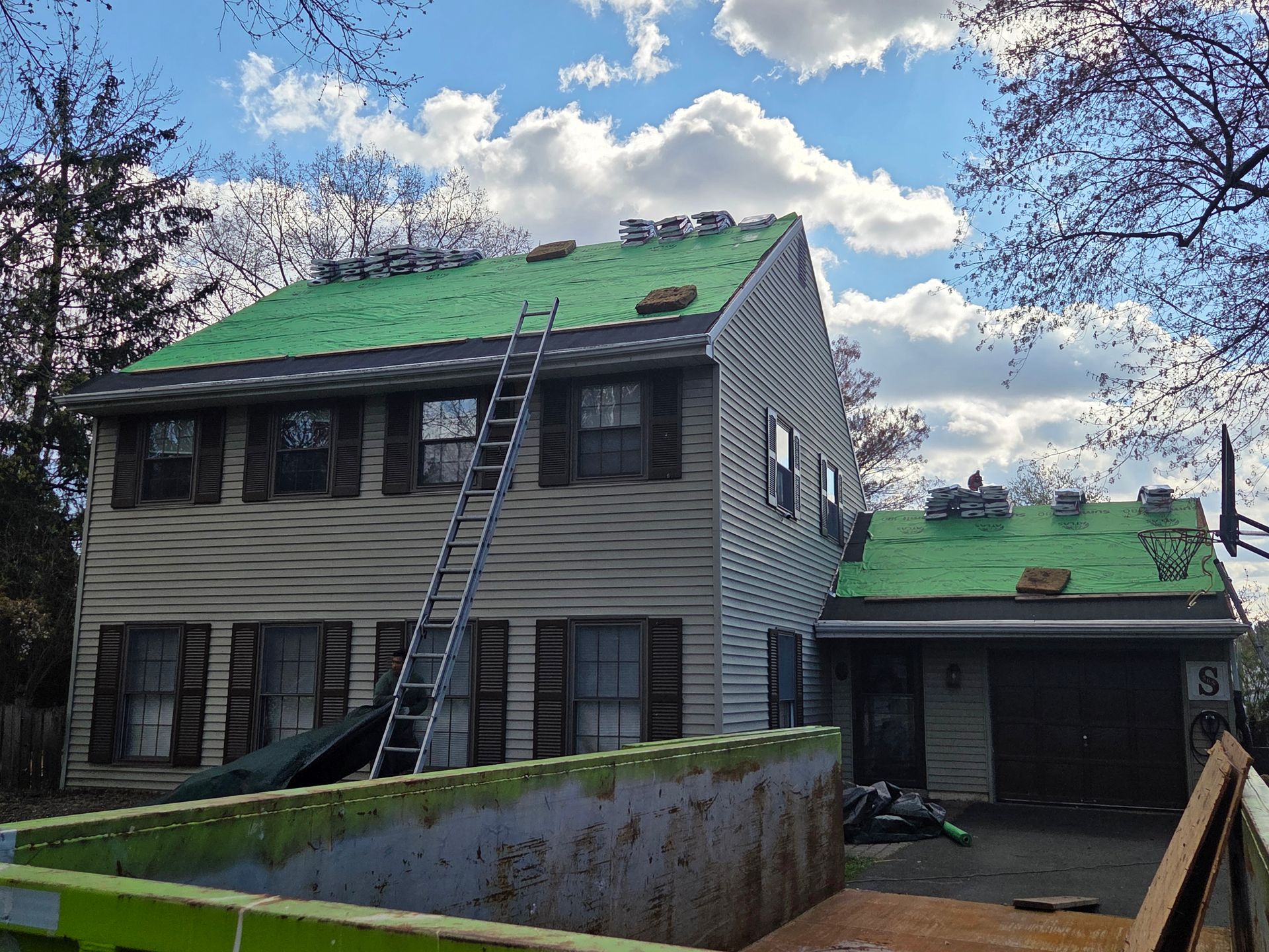 House with green roof being repainted, ladder leaning against the front, under a cloudy sky