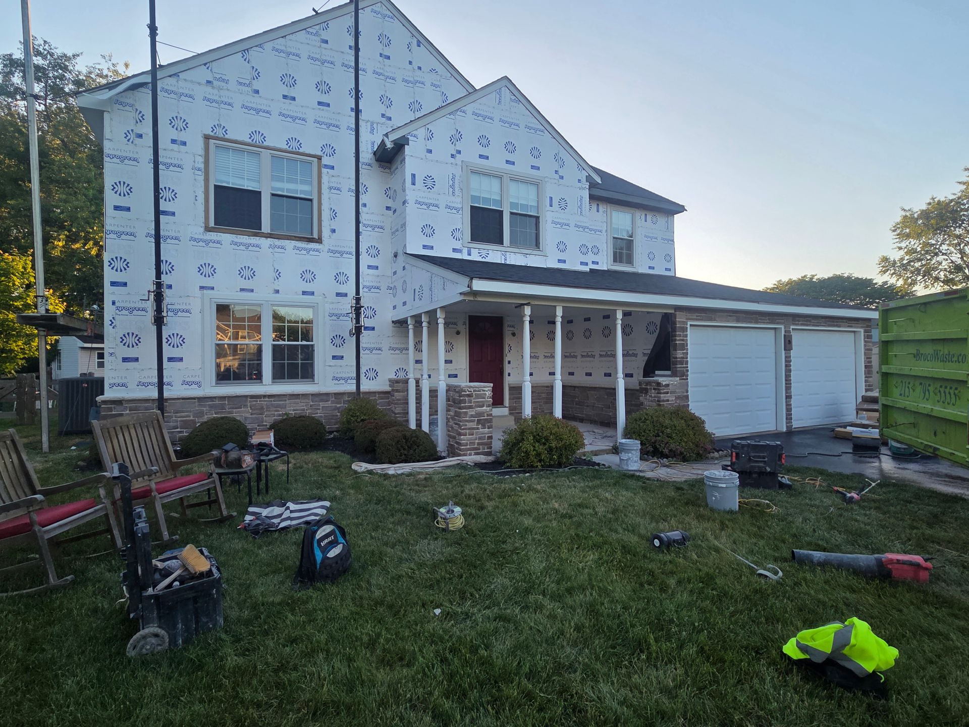 Partially built white two-story house with porch, garage, and construction tools scattered on the lawn.