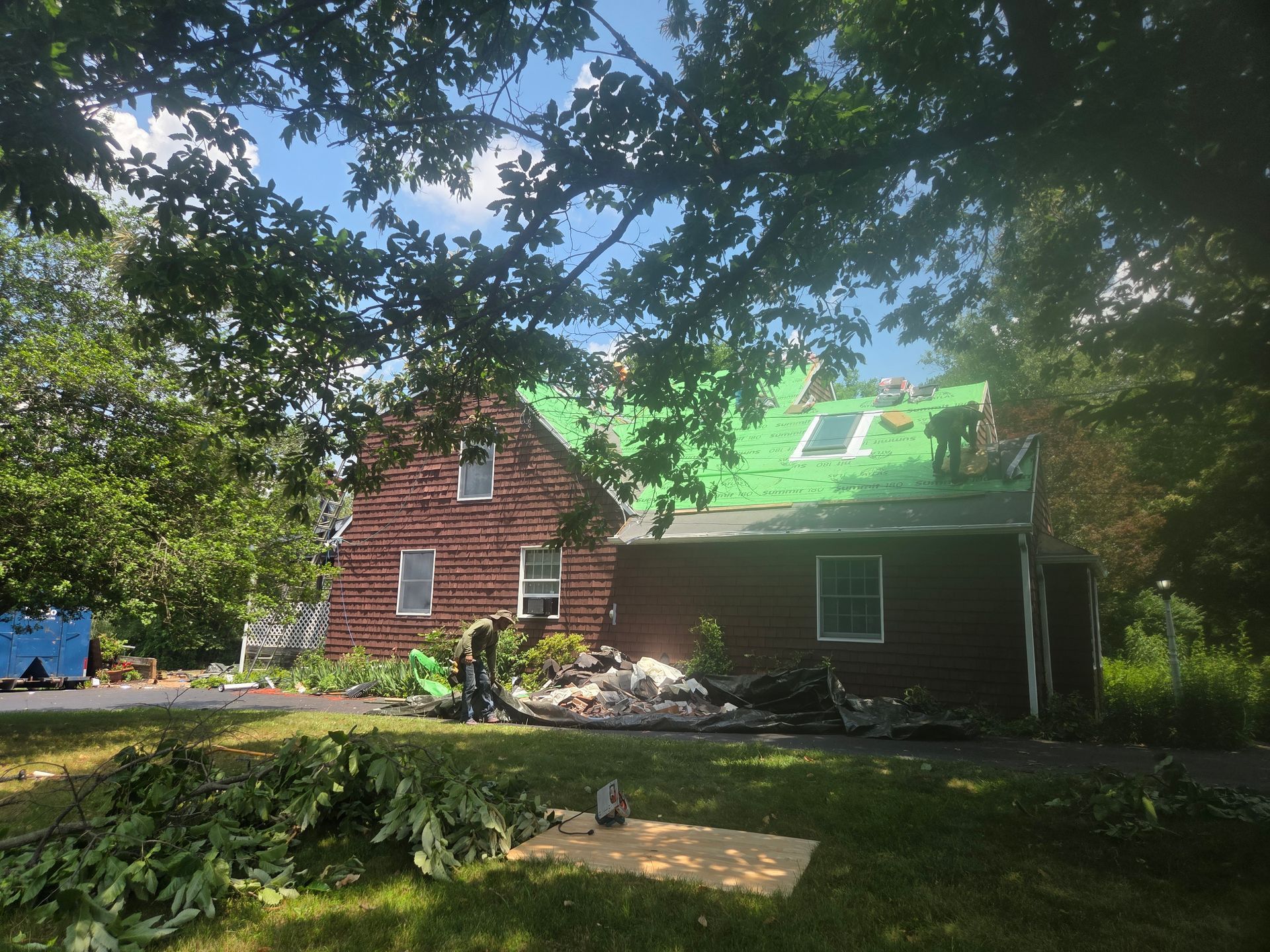 Red house with green roof and side addition beneath trees, in a wooded yard.