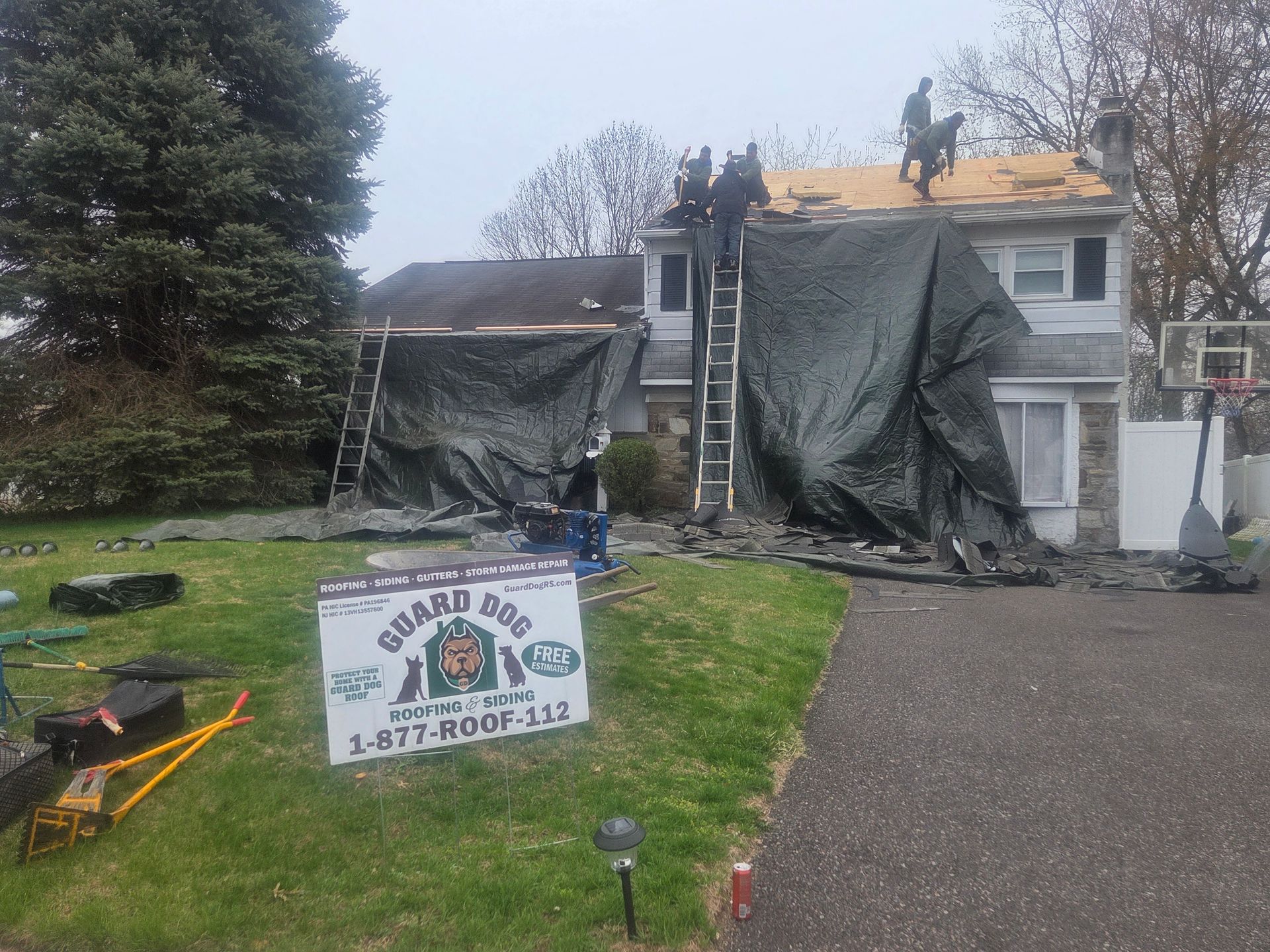 Damaged house with tarp-covered roof and a yard sign for a construction or repair company