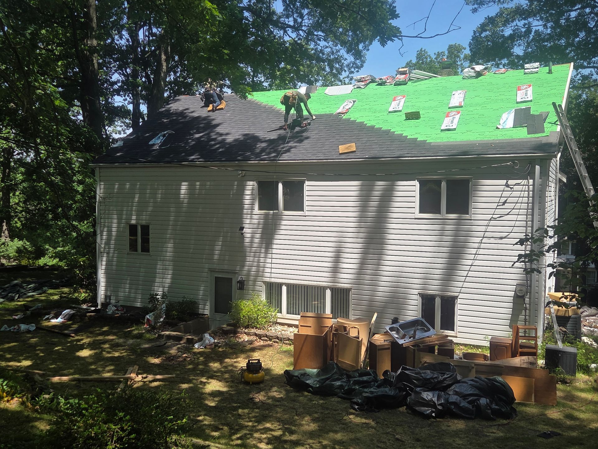House roof under repair with green underlayment, ladders, and materials in the yard