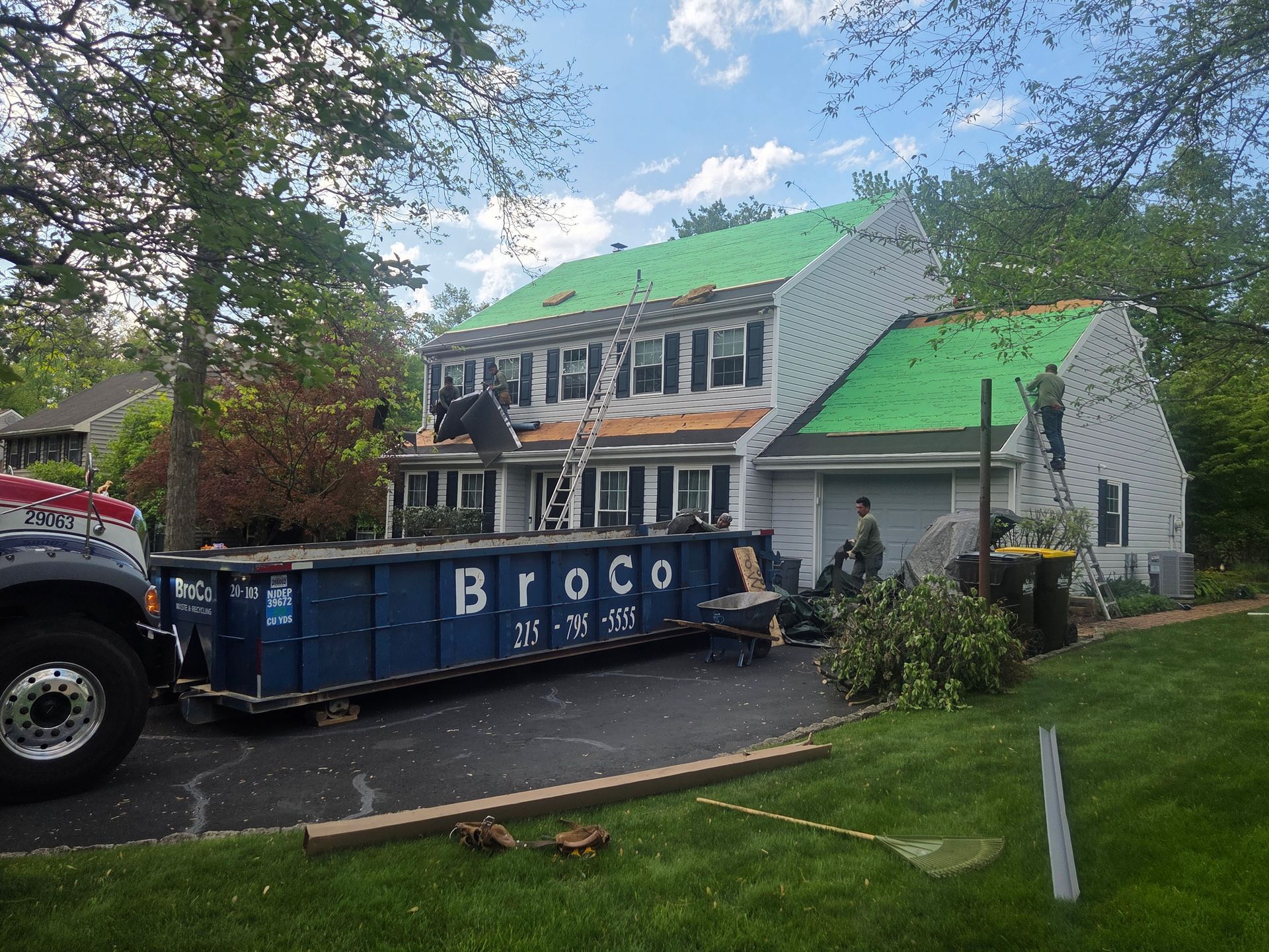 House under repair with green roof tarps and a large blue dumpster in the driveway