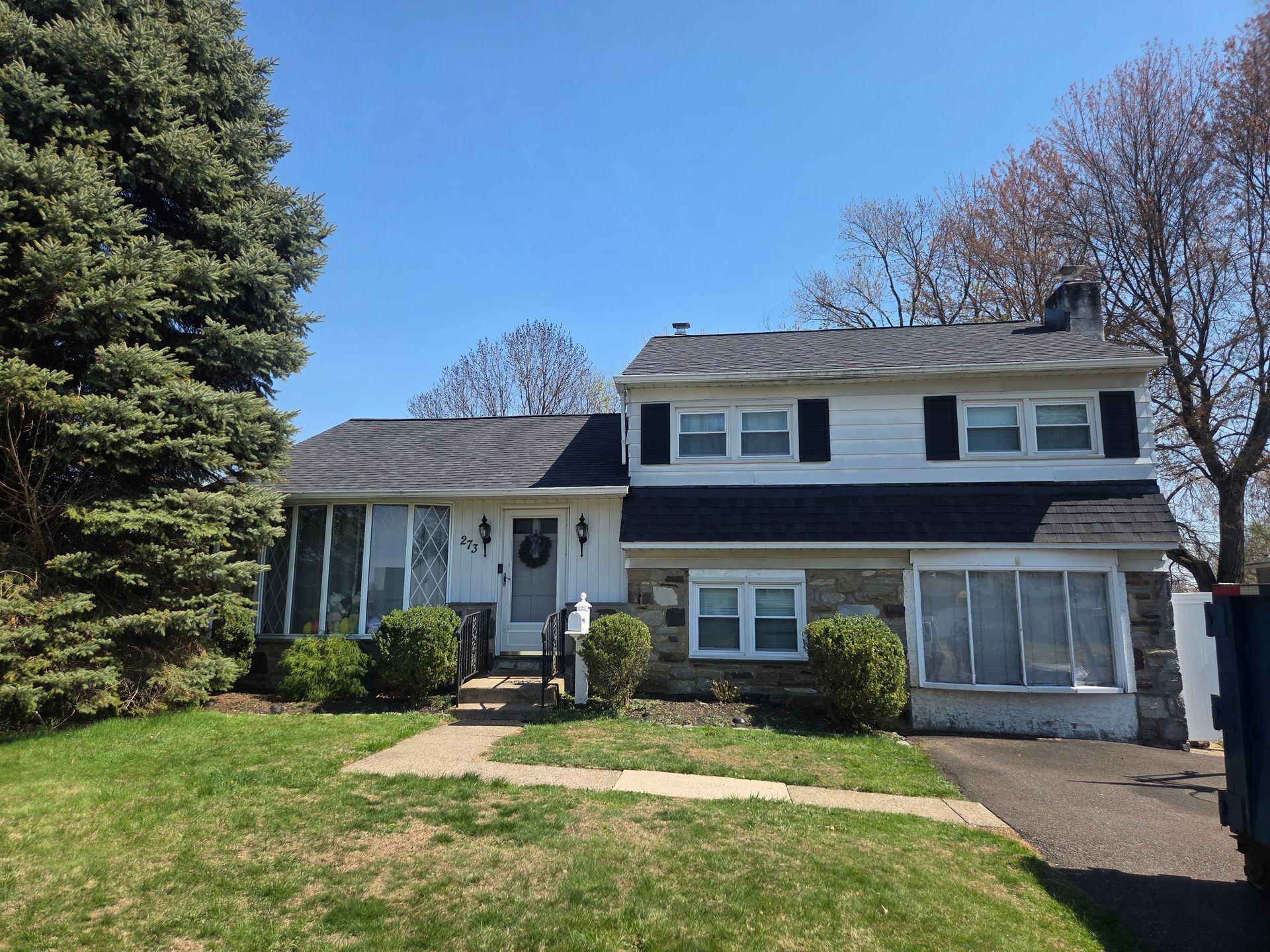 Two-story gray house with white trim, small porch, and green lawn under a clear blue sky.