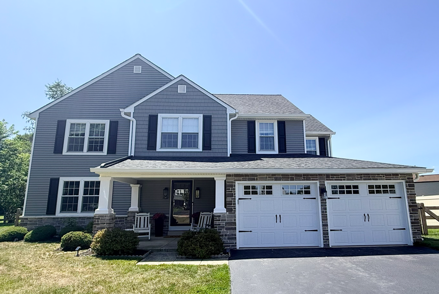 Two-story gray house with white trim and attached two-car garage under a clear blue sky