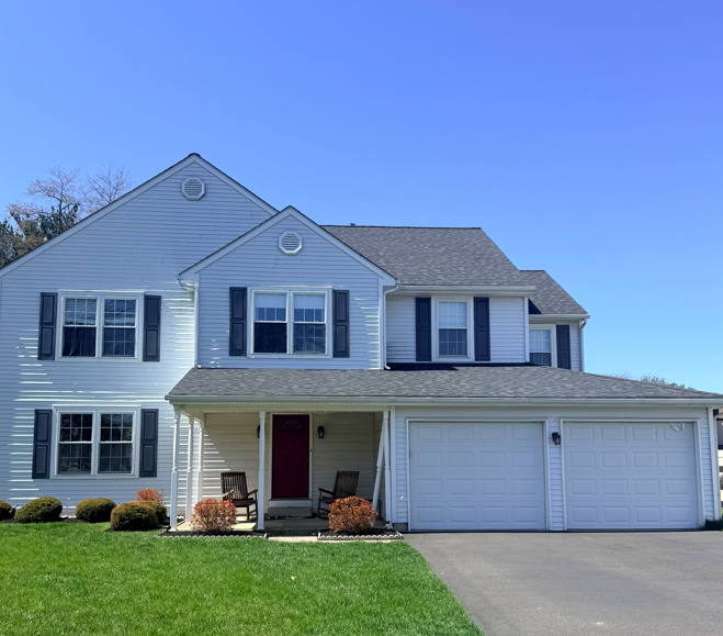 Suburban two-story white house with red front door, attached double garage, and green lawn under a blue sky