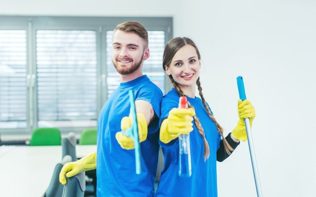 A man and a woman are standing back to back holding cleaning supplies.