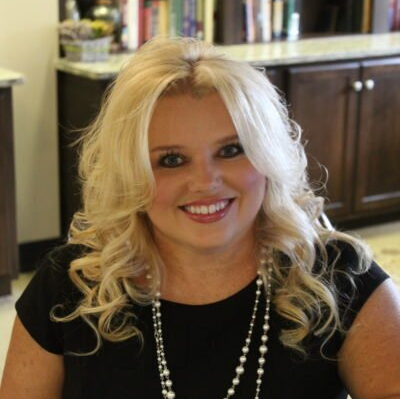 A woman with blonde hair is wearing a black shirt and a pearl necklace