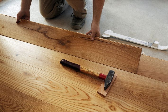 Una persona sta installando un pavimento in legno con un martello sul pavimento.