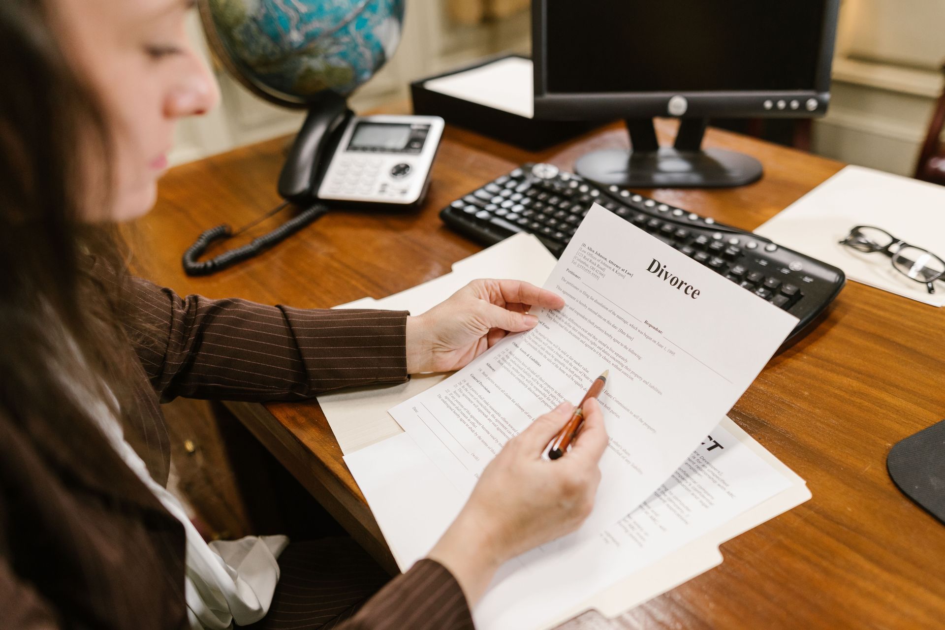 Person reviewing a stack of papers at a desk with a phone and computer in the background
