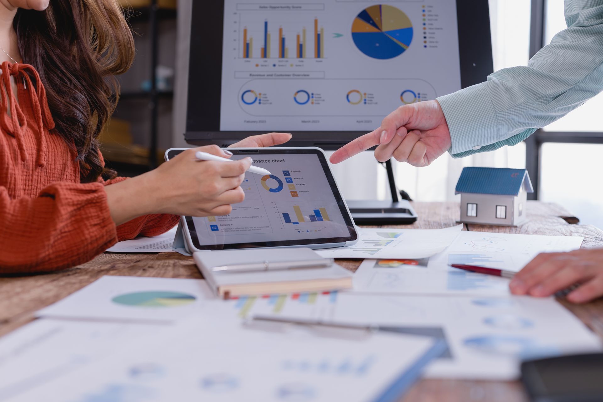 Business meeting with people pointing at a tablet and charts on a presentation screen