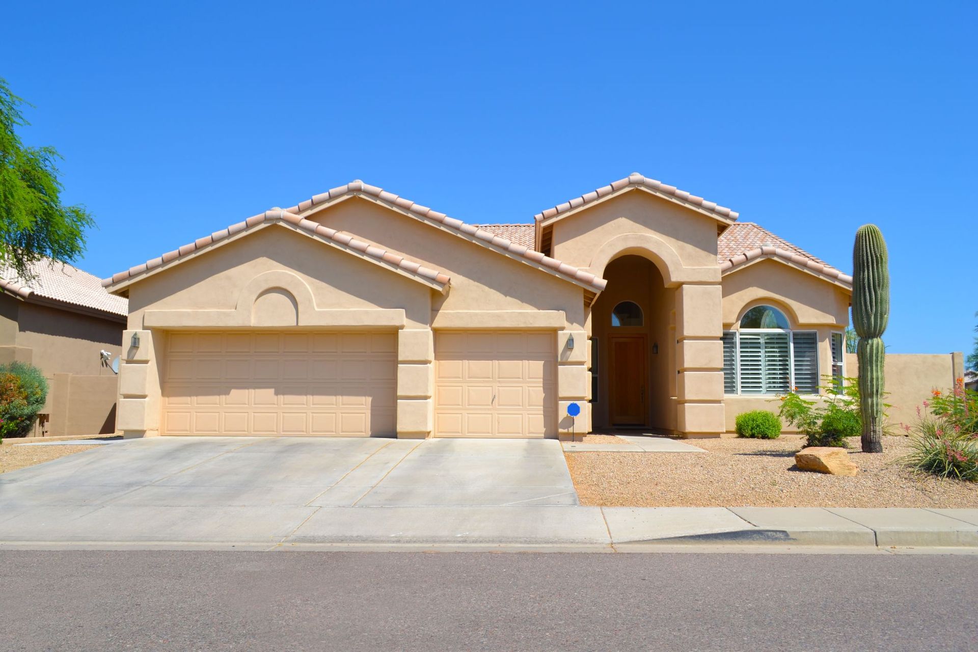 Single-story tan stucco house with a two-car garage and desert landscaping under a blue sky