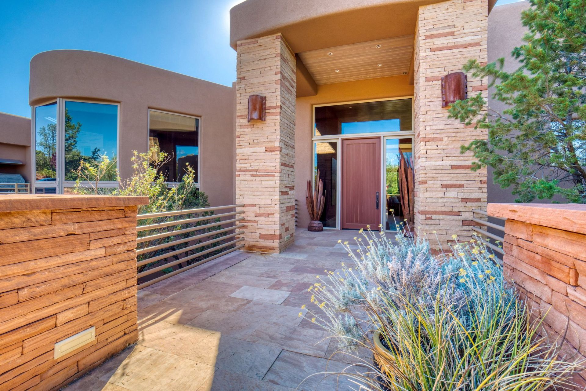 Modern stucco house entrance with stone columns, wooden fence, and desert landscaping
