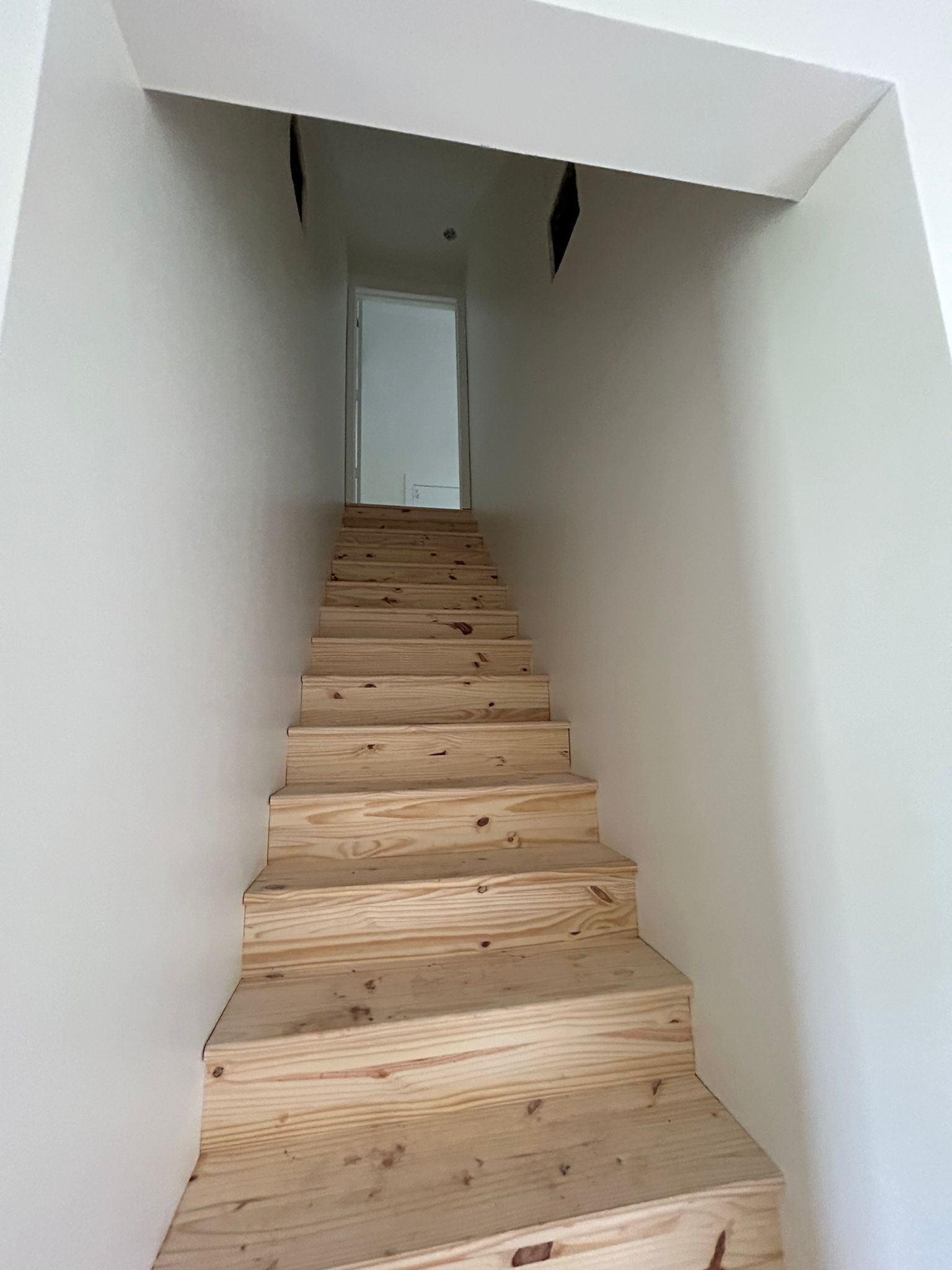 A set of wooden stairs leading up to a white wall.