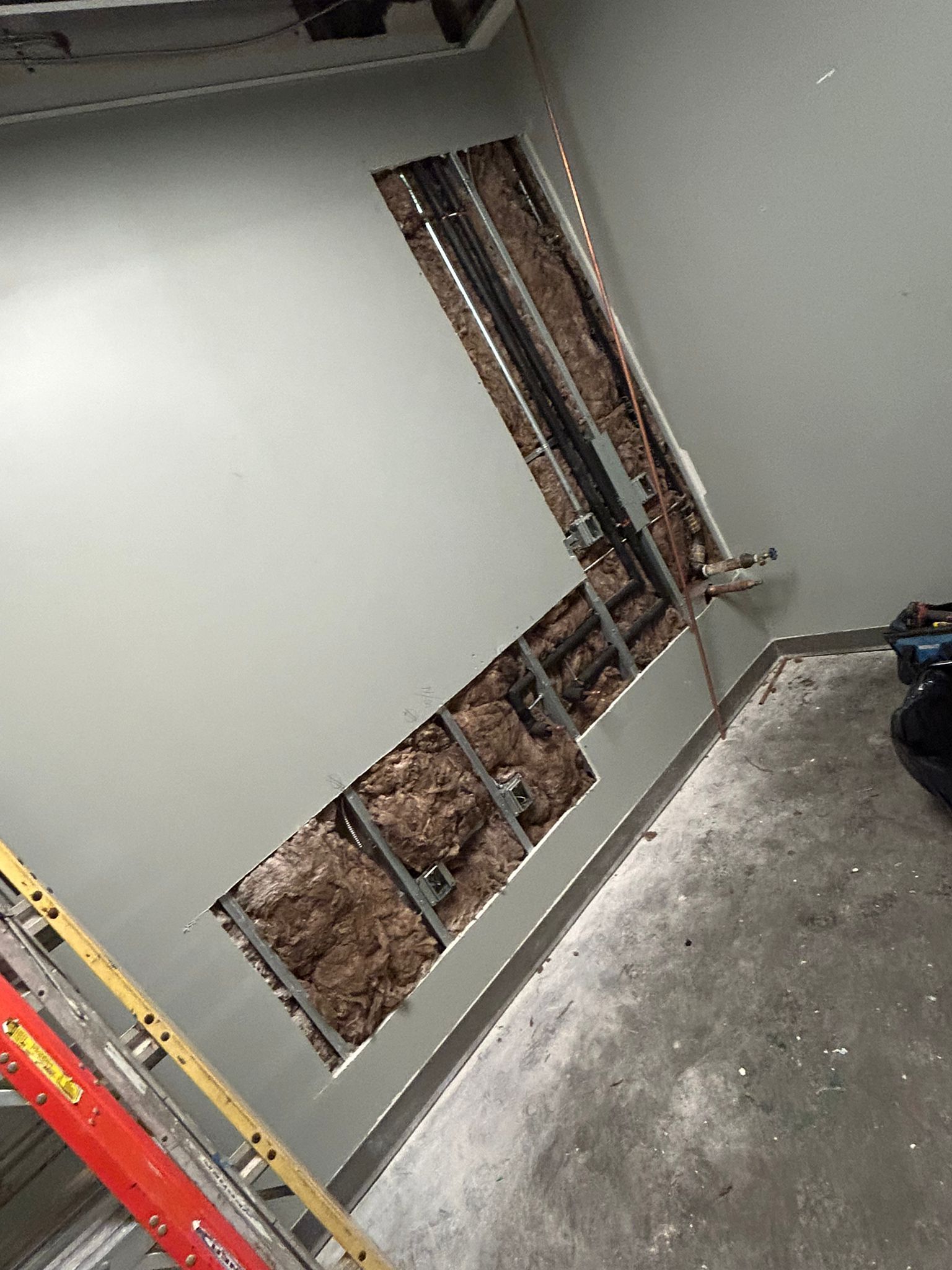 A room with a hole in the wall and a ladder.