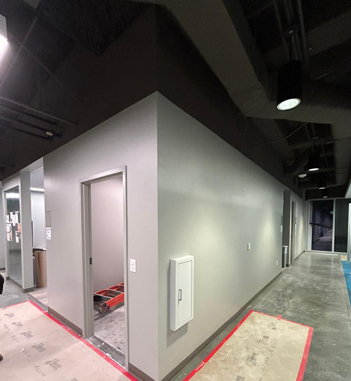Empty industrial hallway with gray walls, open doorway, and black ceiling lights