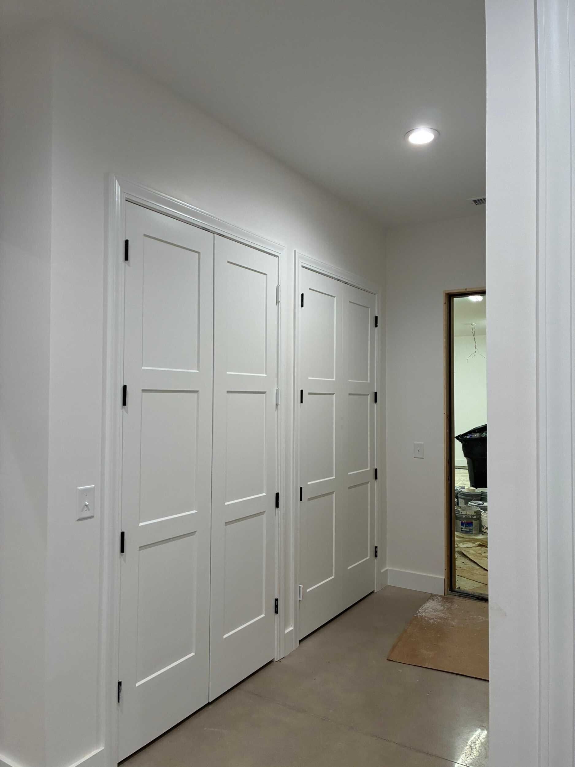 Hallway with white closet doors, recessed light, and a mirror at the end