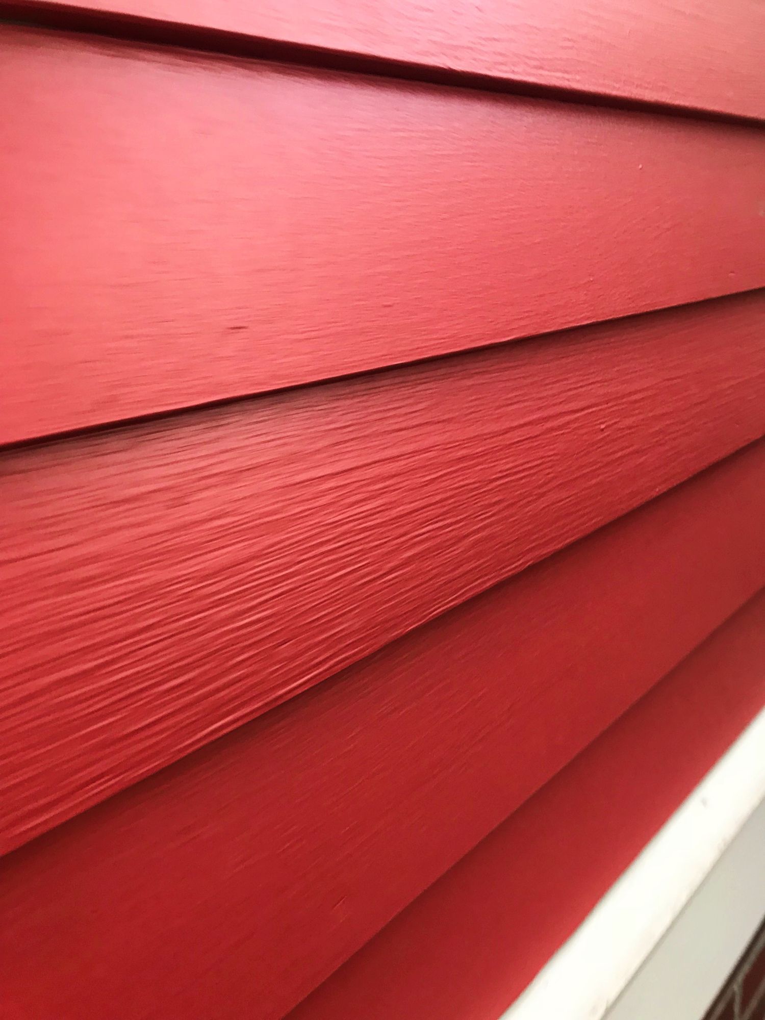 Red painted siding on a building, angled view, showing textured horizontal planks.