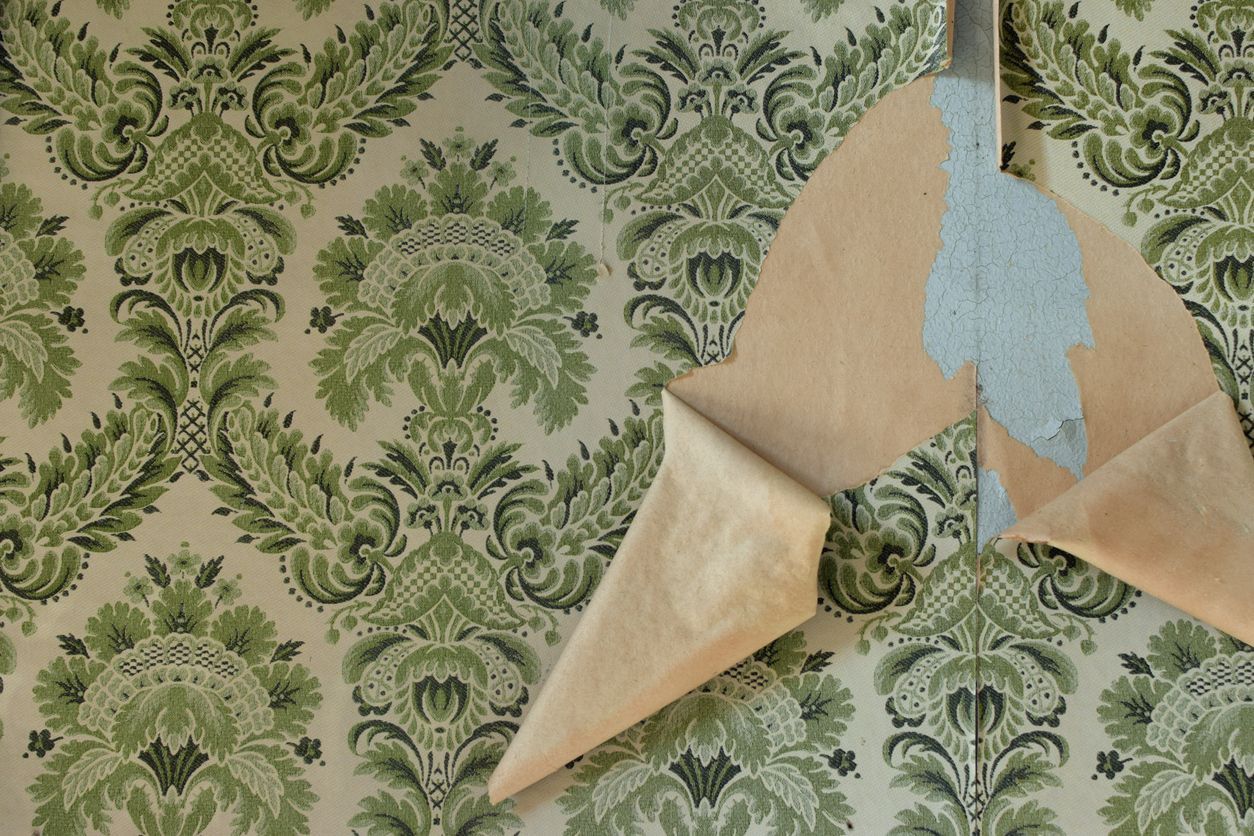 Green damask wallpaper, partially peeled to reveal blue adhesive on the wall.