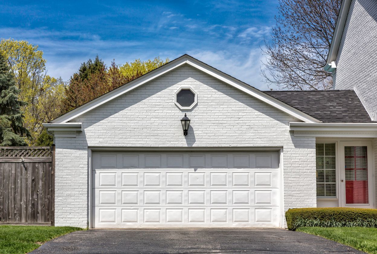 White garage with a closed door, octagonal window, and a section of a house.