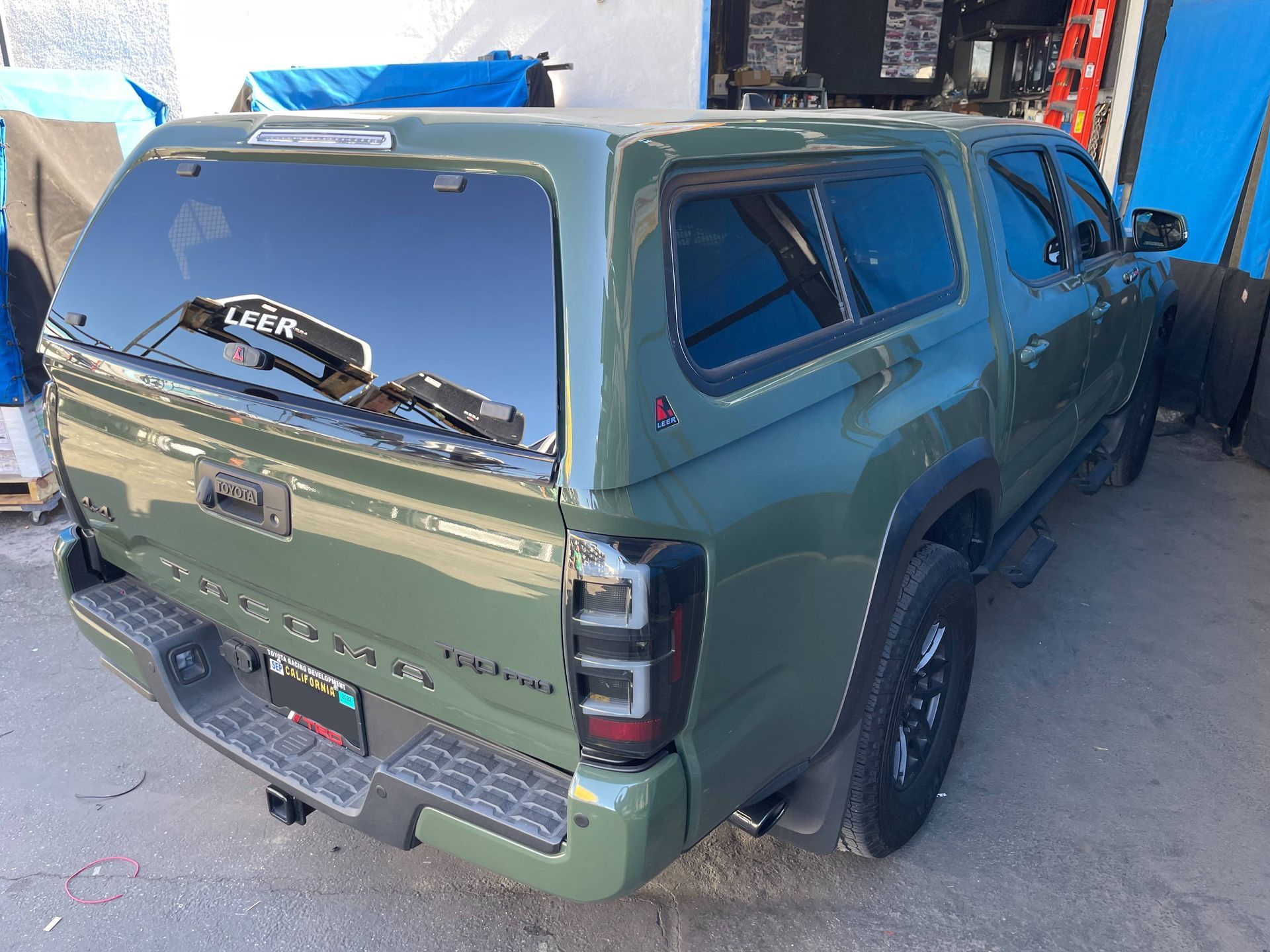 A green truck with a canopy on top of it is parked in a parking lot.