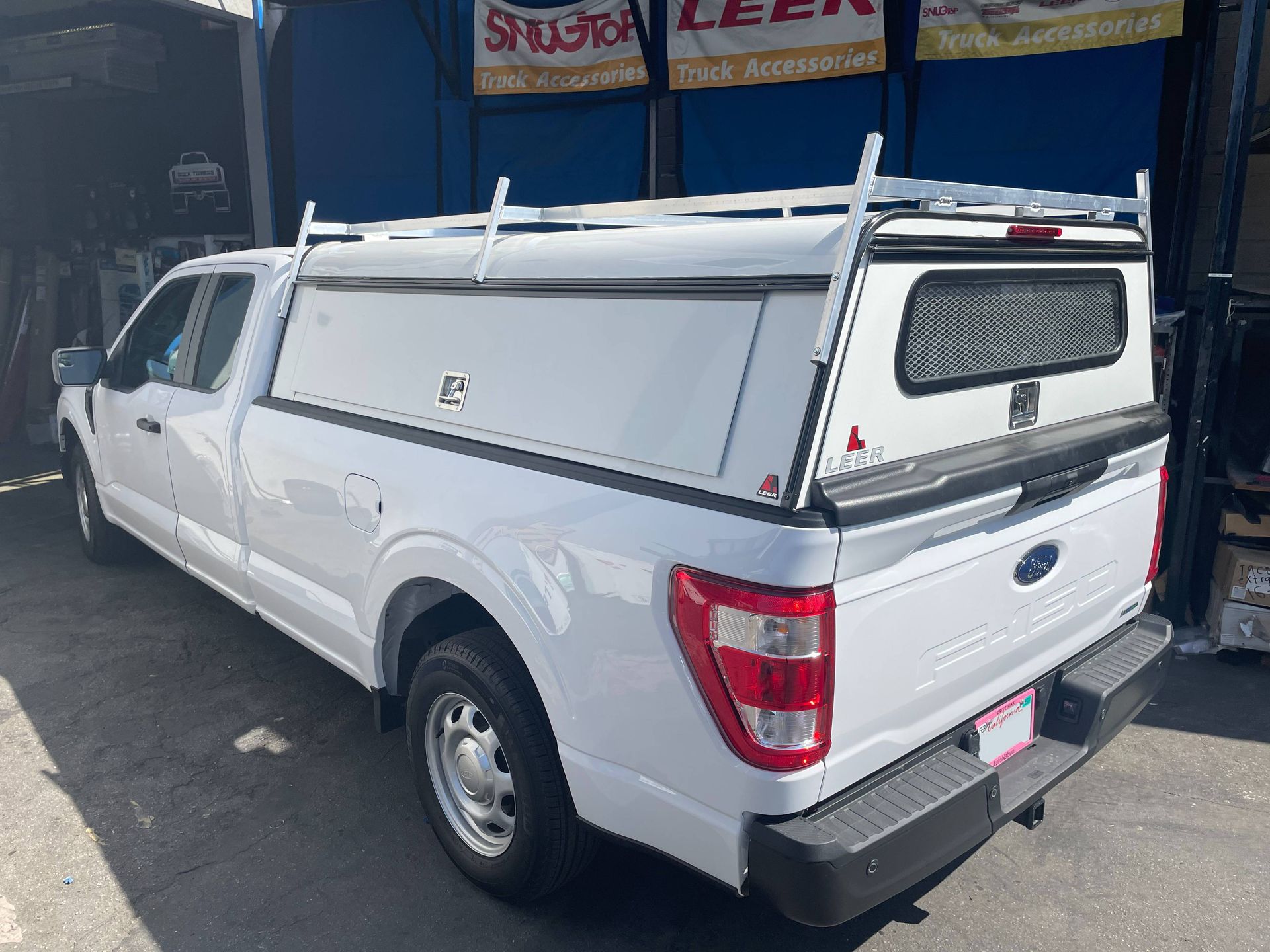 A white truck with a canopy on top of it is parked in front of a building.