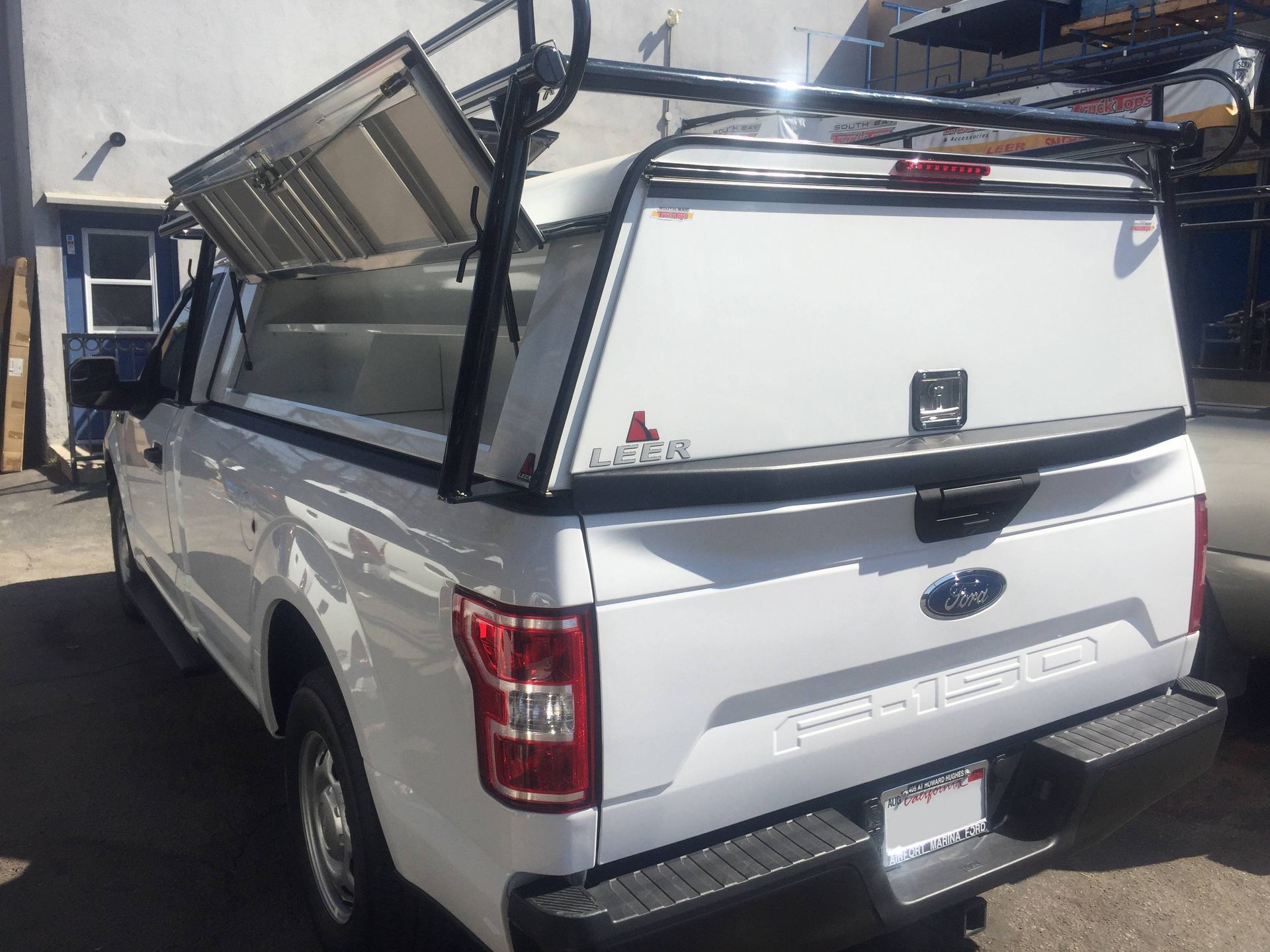 A white truck with a canopy on top of it is parked in front of a building.