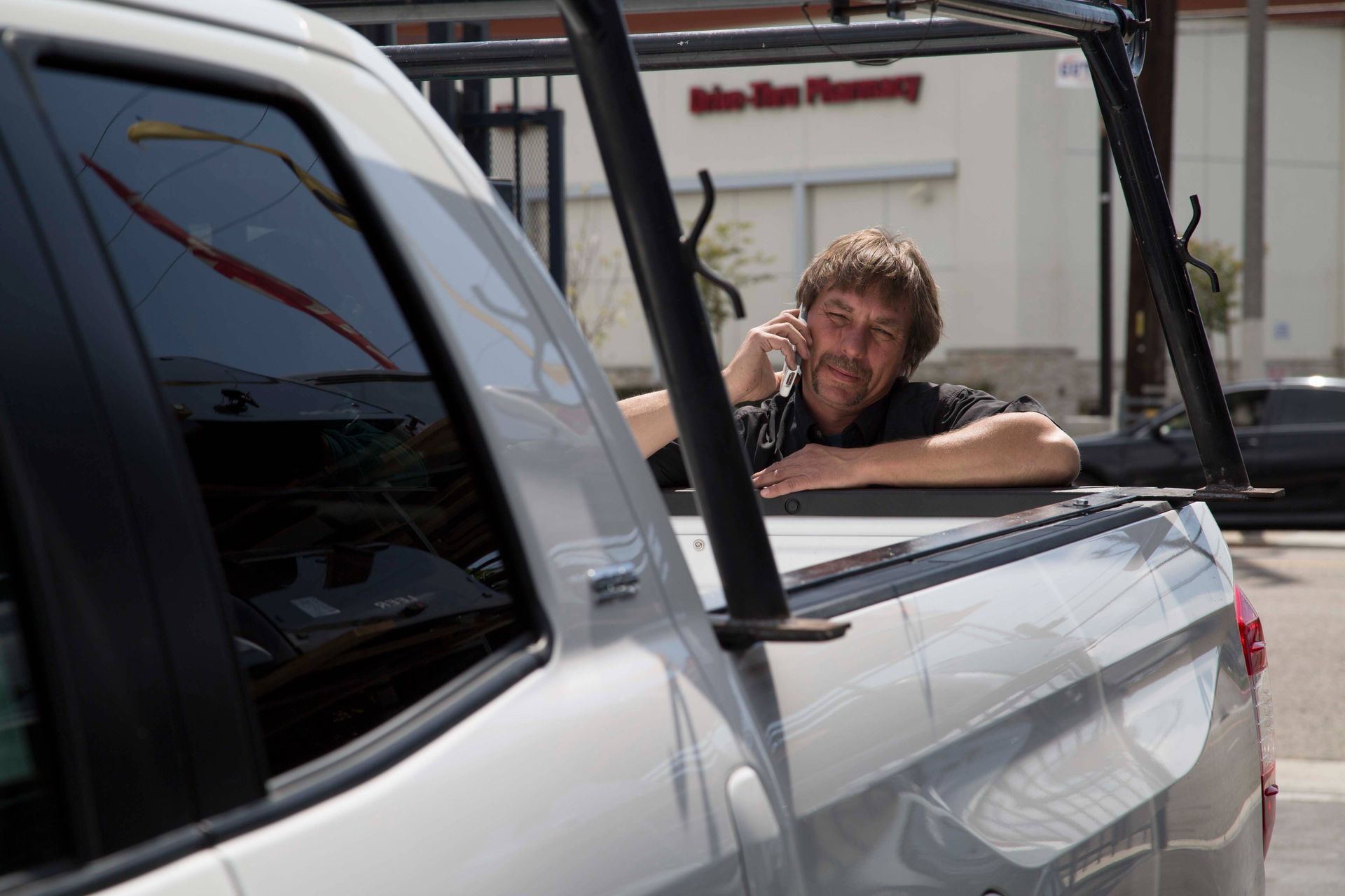 A man leaning on the back of a truck talking on a cell phone.