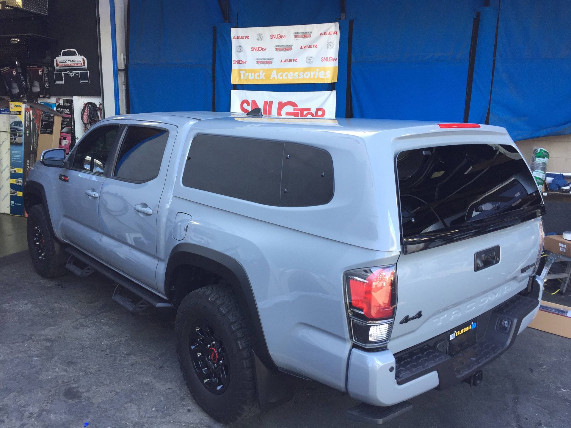 A grey truck with a canopy on top of it is parked in front of a store.