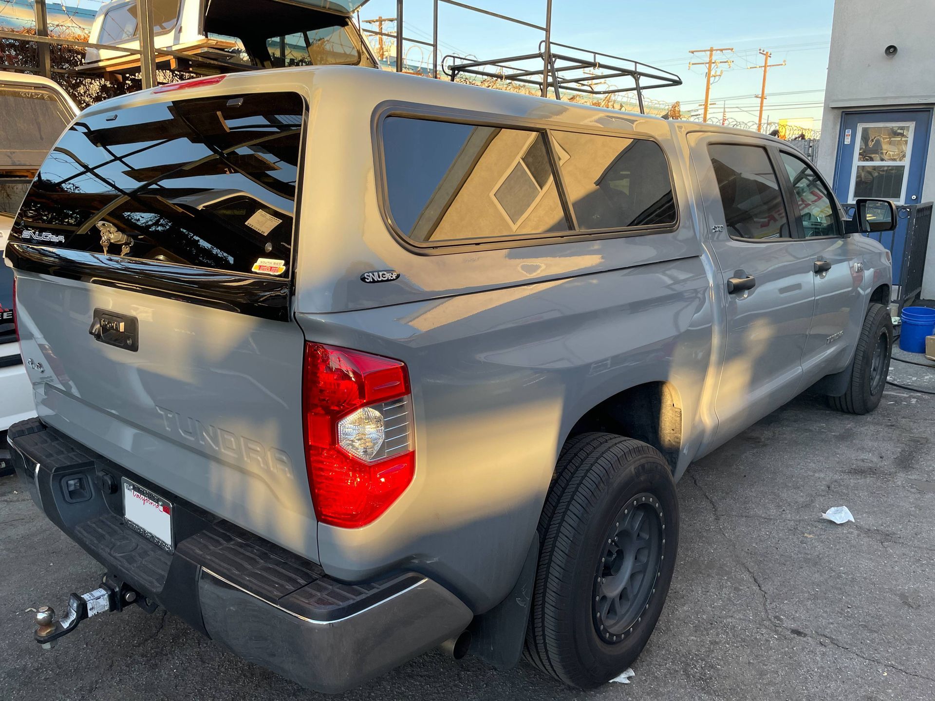 A gray truck with a canopy on top of it is parked in a parking lot.