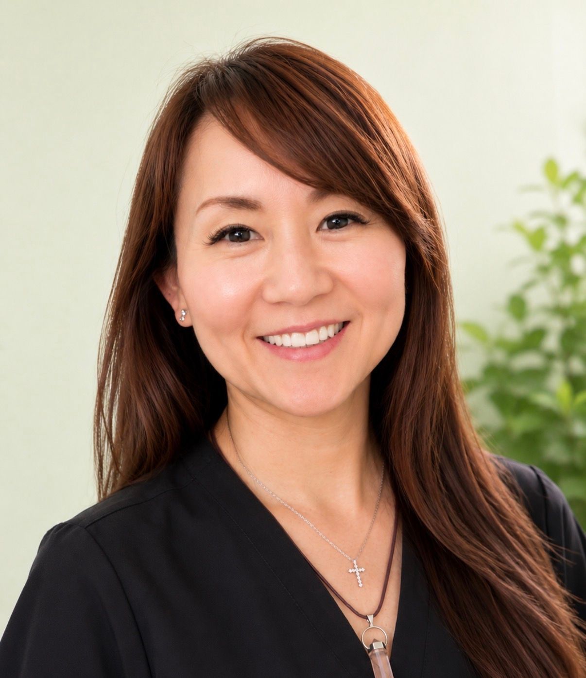 Smiling person with long brown hair wearing a black top, against a light background
