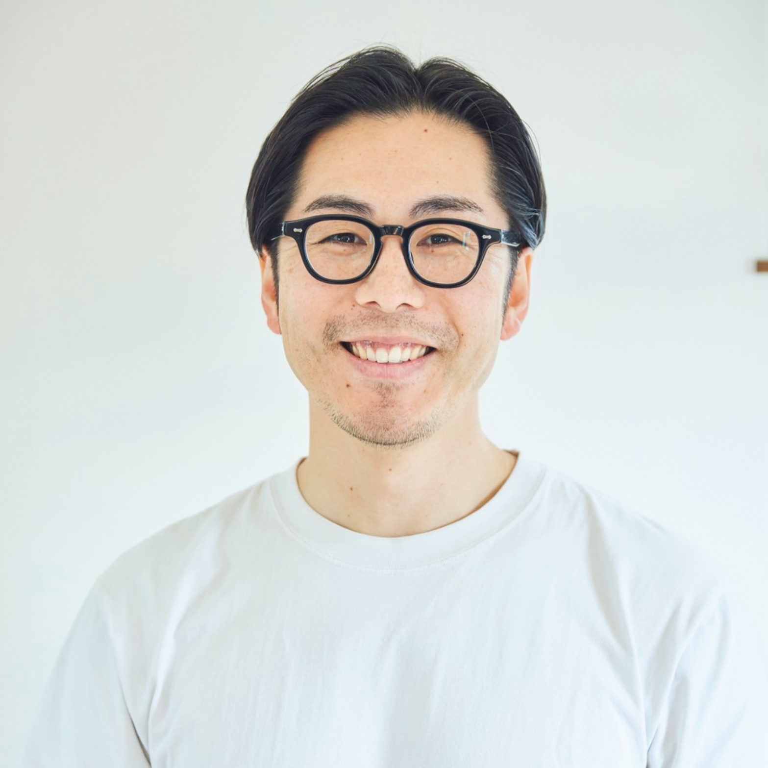 Man wearing glasses and a white t-shirt smiles.