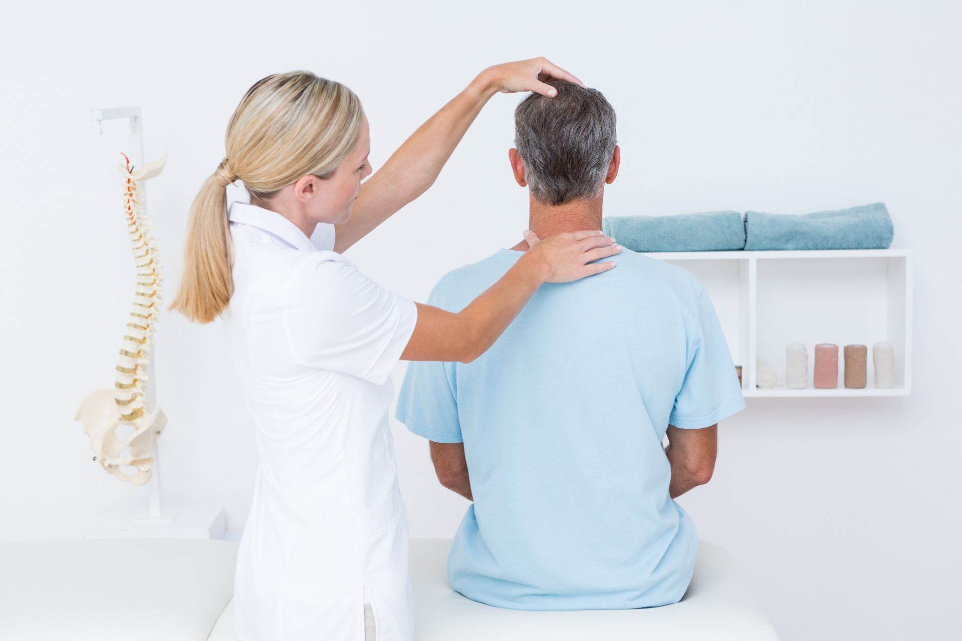 Doctor examining a seated patient’s neck and head in a bright clinic room