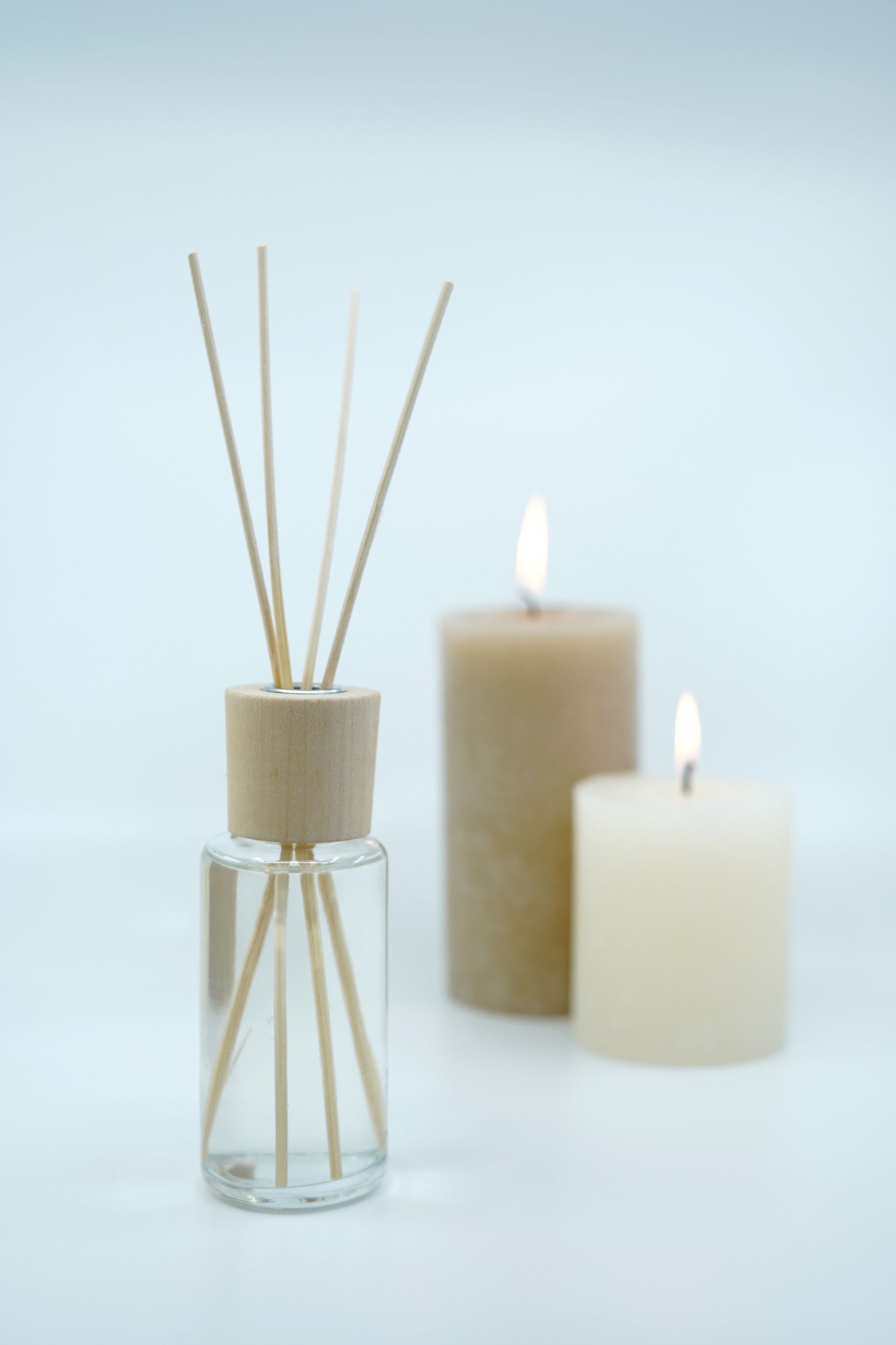 White diffuser bottle with reeds in front of two lit beige candles on a soft background