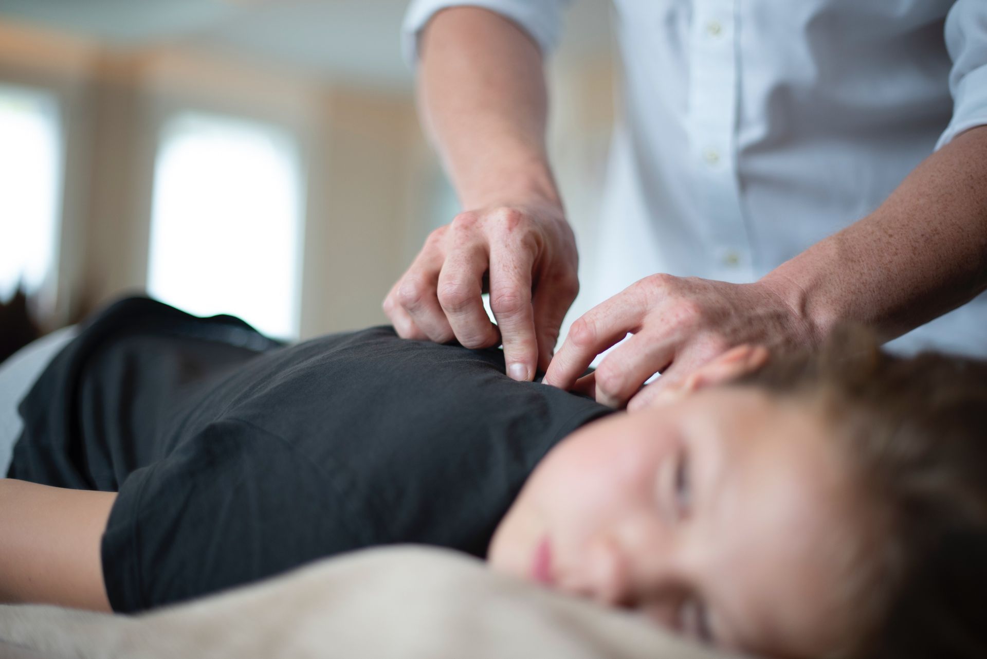 Person receiving a back massage on a table while another person applies pressure near the shoulders