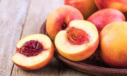 A bowl of peaches on a wooden table with one sliced in half.