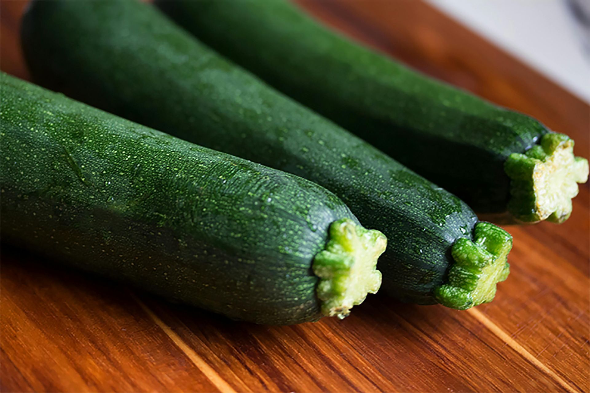 Three zucchini are sitting on a wooden cutting board.