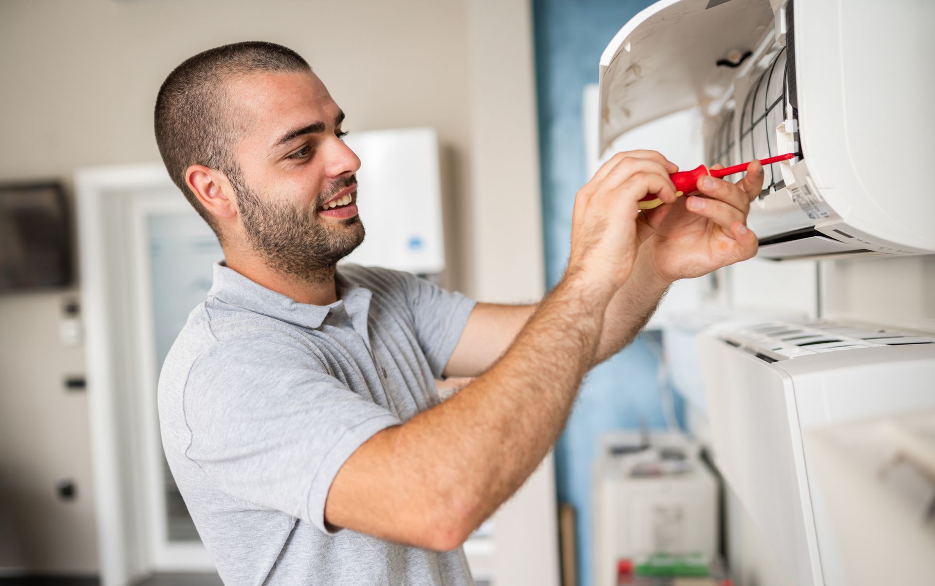 Air conditioning replacement contractor smiling while servicing wall-mounted unit with screwdriver.