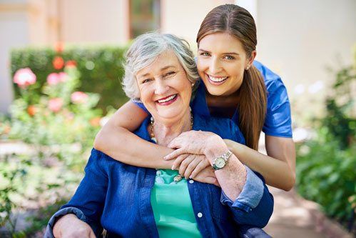 An elderly woman smiling with her granddaughters arms around her