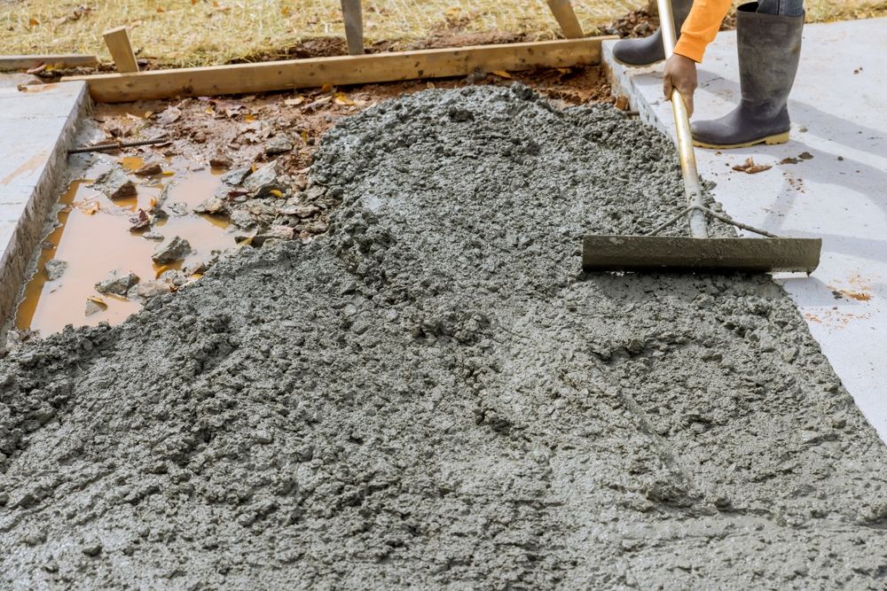 A Man is Spreading Concrete on a Sidewalk With a Rake — Wayne Hall Concreting in South Lismore, NSW