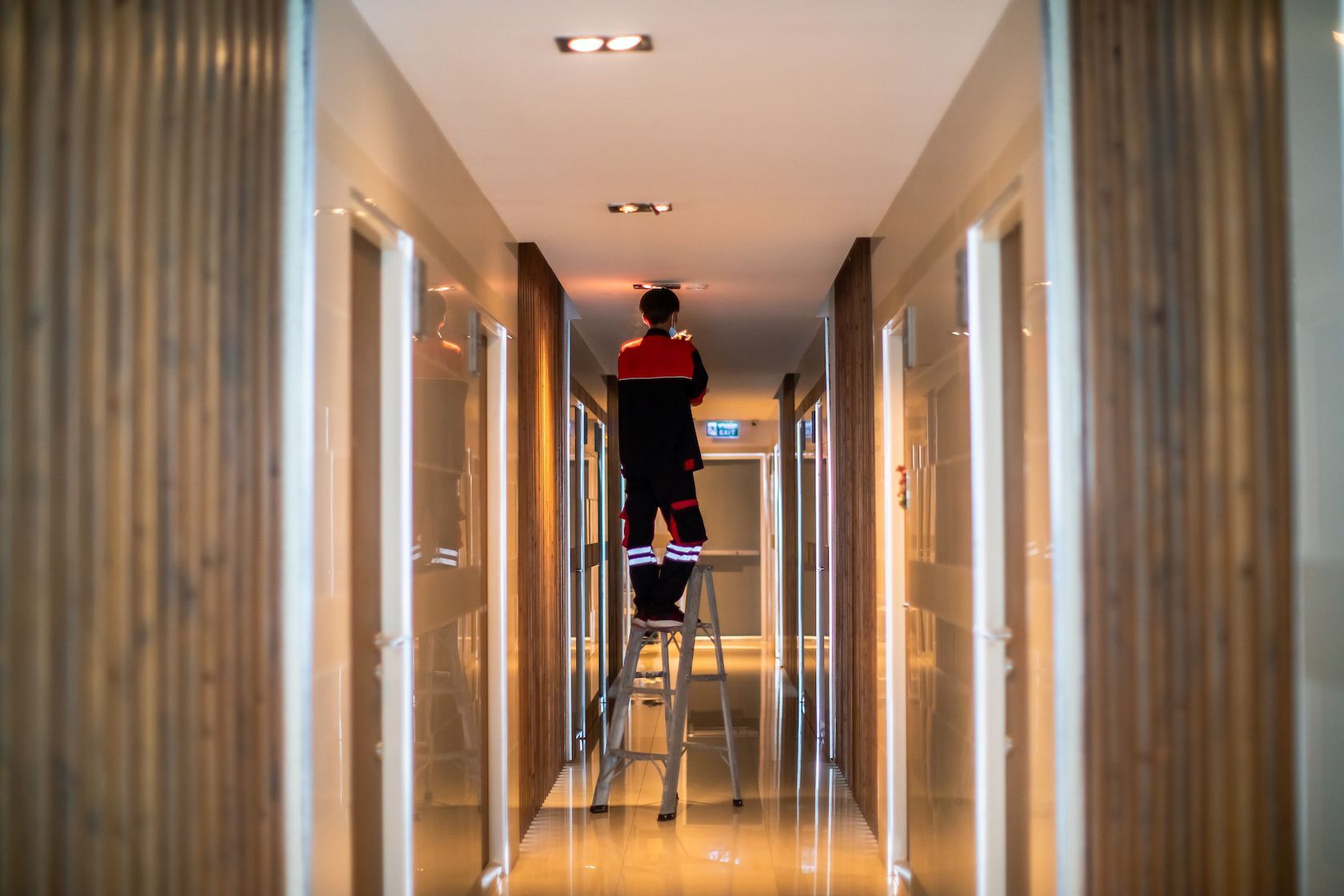 Person Standing on a Stepladder in a Hotel Hallway — Bladz Electrical in Maroochydore, QLD