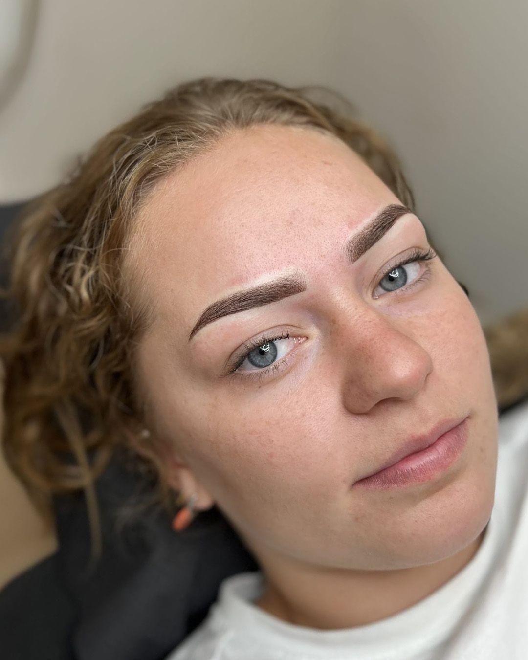Vrouw met recent getatoeëerde wenkbrauwen; bruine strepen en een lichte huid.