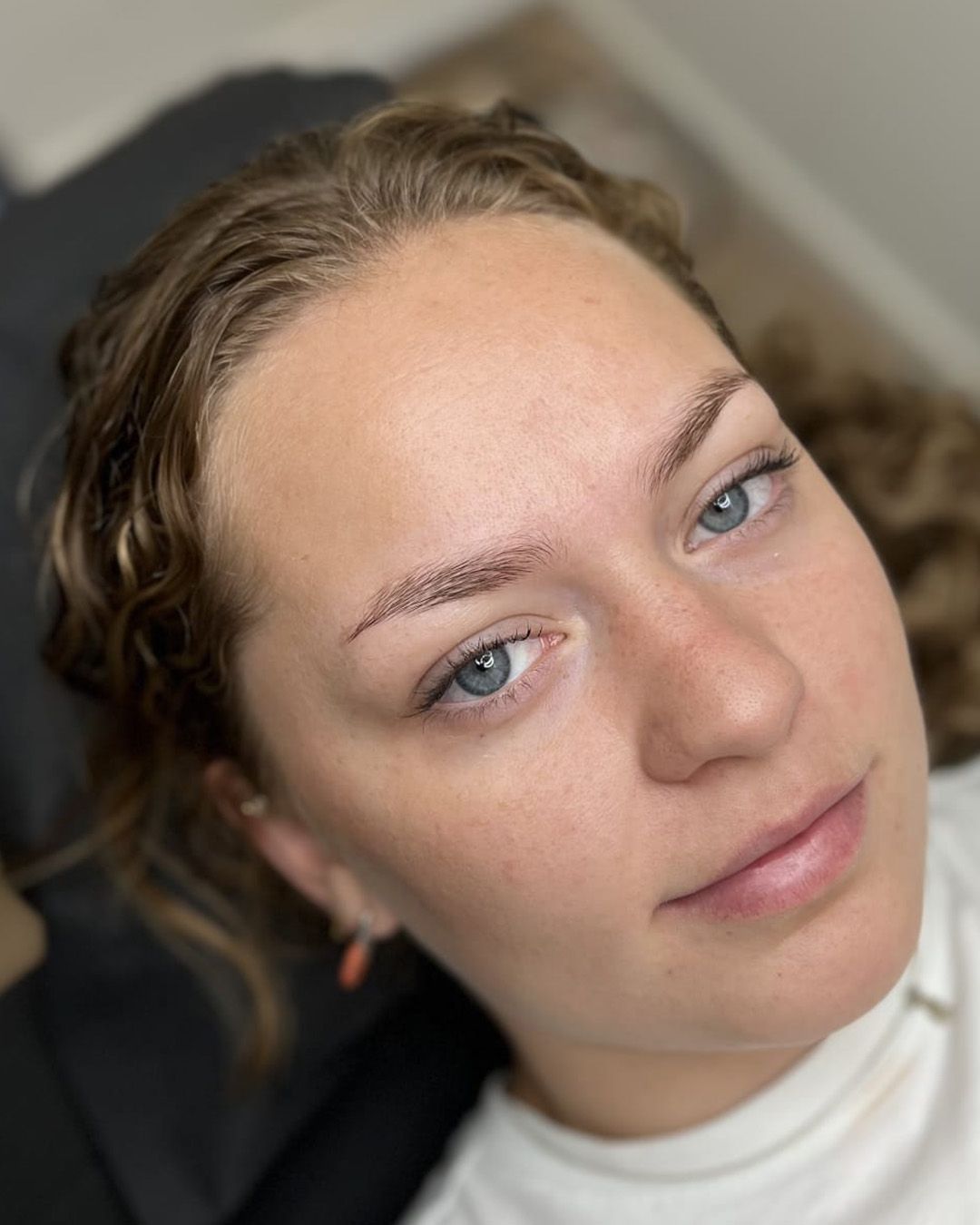 Vrouw voor behandeling getatoeëerde wenkbrauwen kijkt in de camera, lichte huid, lichte ogen.