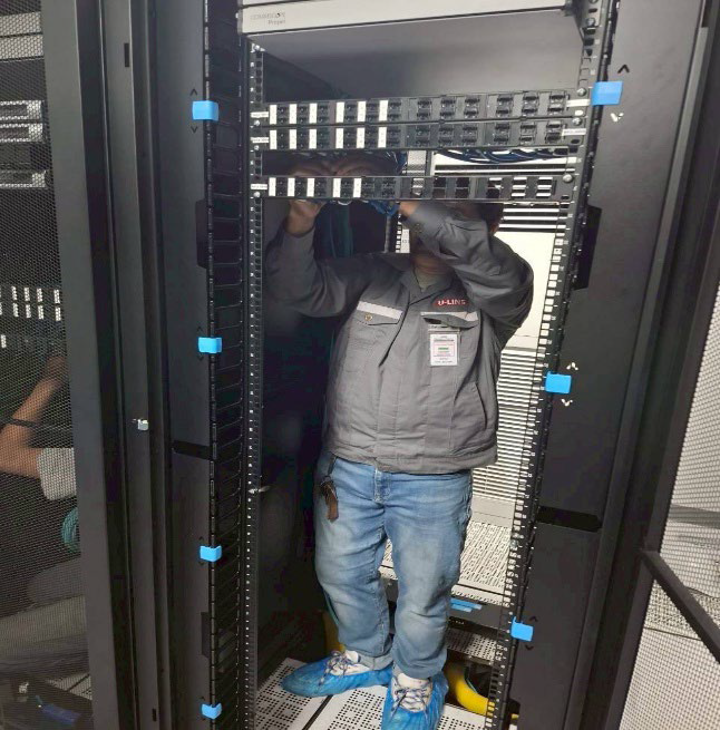 Technician standing inside a server rack, adjusting cables in a data center aisle.