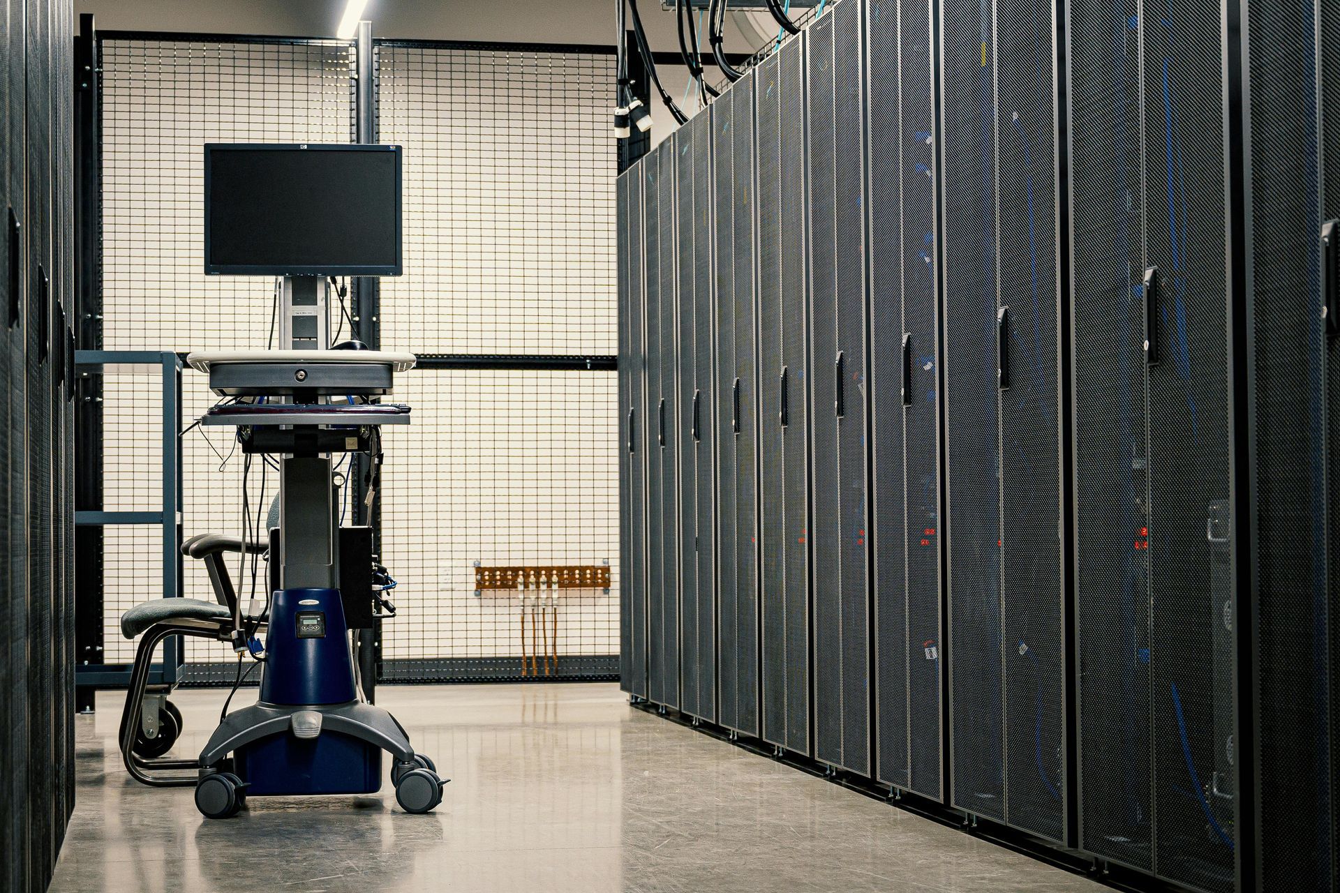 Server room with black server racks and a cart-mounted monitor in the foreground