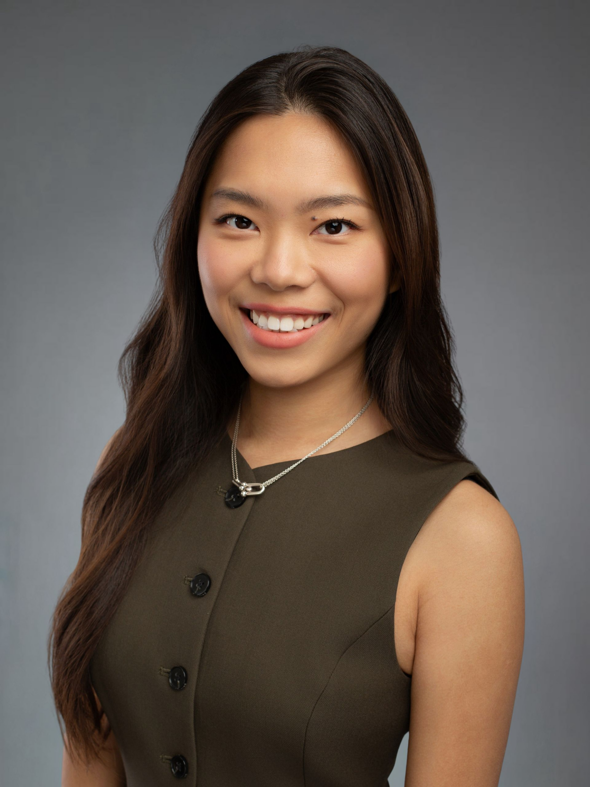 Woman in a green vest smiles at the camera against a gray backdrop.